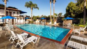 a pool with white chairs and blue umbrellas at Casa Via Mar Inn, Ascend Hotel Collection in Port Hueneme