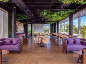 a restaurant with purple couches and tables and windows at Grand Mercure Malang in Malang