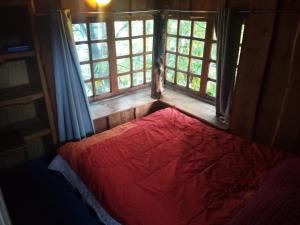 a bedroom with a red bed in a room with windows at Cabañas Llakolen in Neltume