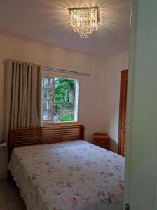 1 dormitorio con cama, ventana y lámpara de araña en Apartamento Vivendas do Eucalipto, en Petrópolis