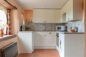 a small kitchen with white cabinets and a microwave at Highdown Farm Holiday Cottages in Cullompton