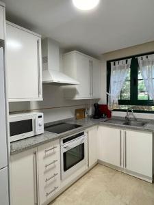 a kitchen with white cabinets and a sink and a microwave at Bonito apartamento con jardín privado in Finestrat