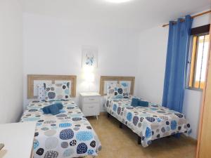 El Rincón de Maruca Primero C في غران تاراغال: سريرين في غرفة ذات أغطية زرقاء وبيضاء