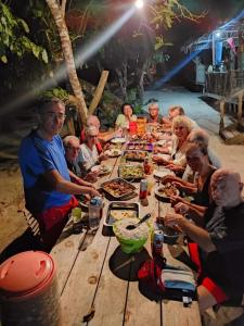 Mambetron Homestay Raja Ampat في Pulau Mansuar: مجموعة من الناس يجلسون حول طاولة خشبية يأكلون الطعام