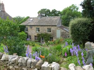 a stone house with a garden with purple flowers at Beckside Cracoe in Skipton