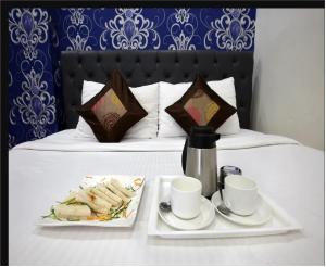 a table with two plates of sandwiches and cups on a bed at Hotel Cross Road By WB Inn in Unnāo