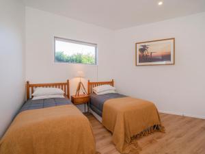 two beds in a room with white walls and a window at Coast Awhile - Whangamata Holiday Home in Whangamata