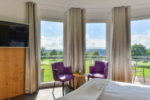 StaufenbergにあるHotel & Golfrestaurant Gut Wissmannshofの紫色の椅子と大きな窓が備わるベッドルーム1室が備わります。