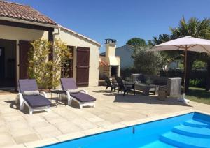 un patio con sillas, una sombrilla y una piscina en La Villa du Payré, proche mer et piscine chauffée, en Jard-sur-Mer