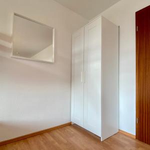 1 dormitorio con armarios blancos y espejo en la pared en Ferienapartment Casa Heideblick mit Sonnenterrasse & Garten, en Radeberg