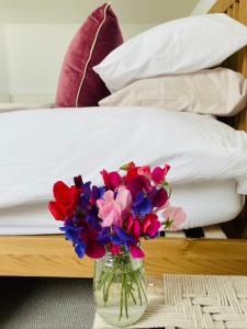 un jarrón de flores sentado en una mesa junto a una cama en Barn Cottage -Westerlands en Graffham