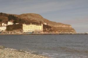 a building on the shore of the water with a mountain at Spacious cosy apartment in Llandudno