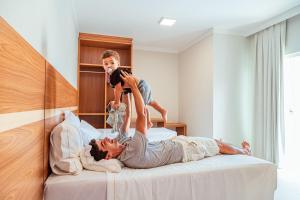 a boy playing on top of a bed with a woman at Orquídeas Praia Hotel in Porto Seguro