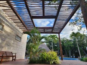 a patio with a wooden roof with a bench and trees at Hermoso condominio con alberca en Puerto Morelos in Puerto Morelos