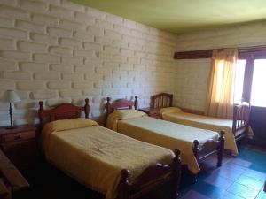 Un dormitorio con 2 camas y una pared con ventanas. en Hotel El Jardin Dante en Tilcara