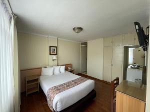 um quarto de hotel com uma cama branca e uma televisão em Hotel Premier em Tacna