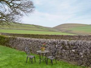 a table and two chairs in front of a stone wall at Sweet knoll cottage in Buxton