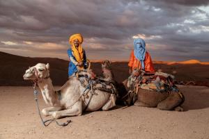 two people riding on the backs of camels in the desert at Alkamar Camp Agafay in El Karia