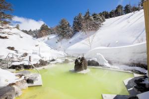 a hot spring in the snow with snow covered mountains at Manza Kogen Hotel in Tsumagoi