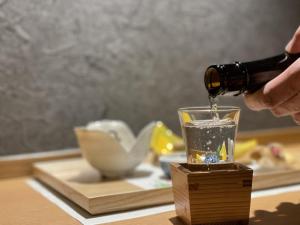 een persoon die een drankje in een glas giet op een tafel bij Yukemuri no Yado Inazumi Onsen in Yuzawa