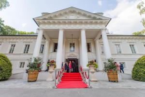 um grupo de pessoas em pé em um tapete vermelho em frente a um edifício em Hotel & Spa Pałac Mała Wieś em Mała Wieś