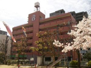 Urban Life Matsuda - Vacation STAY 85183 في أوكاياما: مبنى أحمر كبير مع أشجار اكورا أمامه