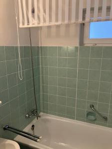 baño de azulejos verdes con bañera y ventana en Gemütliches 1 Zimmer Appartement, en Langelsheim