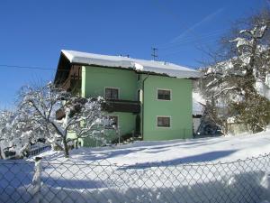ein grünes Haus hinter einem Zaun im Schnee in der Unterkunft Arlbergsun in Pettneu am Arlberg