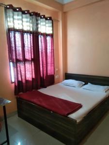 a bedroom with a bed with a window with red curtains at Hotel Hansa Palace by WB Inn in Kānpur