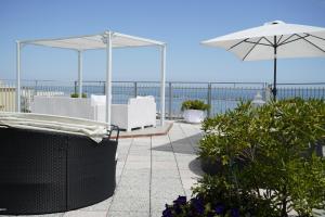 un patio con sillas blancas, una sombrilla y el océano en Hotel Embassy, en Cesenatico