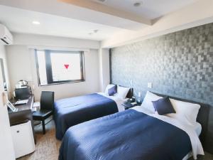 a hotel room with two beds and a desk and a window at HOTEL LiVEMAX Hachioji Ekimae in Hachioji
