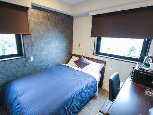 a bedroom with a bed and a desk and two windows at HOTEL LiVEMAX Hachioji Ekimae in Hachioji