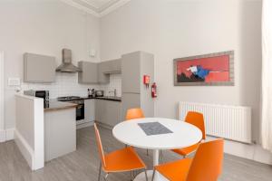 cocina y comedor con mesa blanca y sillas naranjas en Southside Apartments by Destination Edinburgh, en Edimburgo
