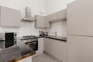 La cuisine est équipée de placards blancs et d'un four avec plaques de cuisson. dans l'établissement Southside Apartments by Destination Edinburgh, à Édimbourg