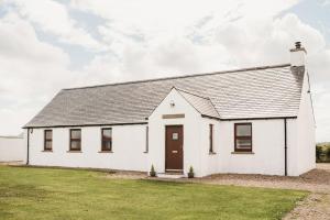 una casa blanca con un techo gris y un campo de césped en The Shepherd's Rest en Thurso