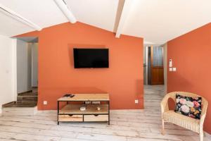 een woonkamer met een oranje muur en een tv bij Le marronnier 2 in LʼIsle-sur-la-Sorgue