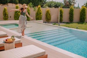 a woman in a hat standing next to a swimming pool at Marble Luxury Suites in Karteros