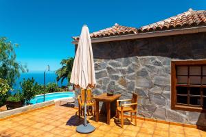 eine Terrasse mit einem Sonnenschirm, einem Tisch und Stühlen in der Unterkunft One bedroom villa with sea view private pool and furnished garden at Tijarafe in Tijarafe