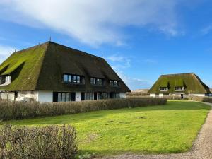 zwei strohgedeckte Gebäude mit Grasdächern auf einem Feld in der Unterkunft Passat in Wenningstedt-Braderup