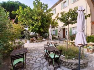 um pátio com mesas e cadeiras e um guarda-sol em Hôtel Le Siècle em Mazan