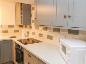 a kitchen with white cabinets and a microwave at Firkin Cottage in Bedale