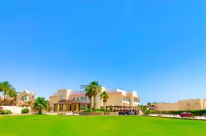 a green park in front of a building with palm trees at Ivy Cyrene Island Resort in Sharm El Sheikh