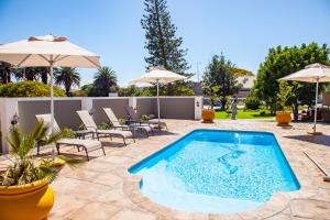 a swimming pool with chairs and umbrellas on a patio at Avanti Guest Lodge in Vredenburg