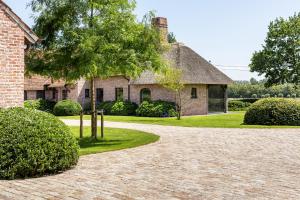una casa de ladrillo con un árbol y una entrada en Hoeve den Akker - luxueuze vakantiewoningen met privétuinen en alpaca's nabij Brugge, Damme, Knokke, Sluis en Cadzand en Damme