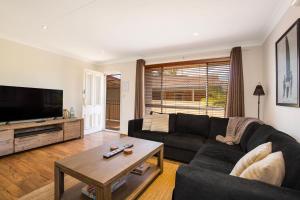 a living room with a black couch and a tv at Sunbaker Pet Friendly Awards Finalist 4 Mins Walk to Culburra Beach in Culburra Beach