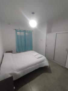 1 dormitorio con cama blanca y cortina azul en Departamentos Mora en General Alvear
