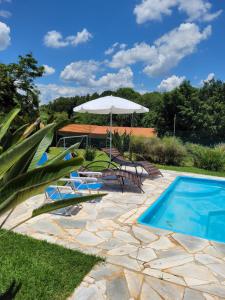 un patio con sombrilla y piscina en POUSADA Chacara ENTRE NÓS en Holambra