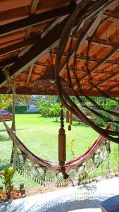 a hammock under a wooden roof with a field of grass at Casa temporada na praia Joia do Atlântico - Ilhéus - Ba in Ilhéus
