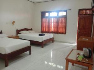 a bedroom with two beds and a table and a window at Batu Jaran Hill Cottage Uluwatu in Uluwatu