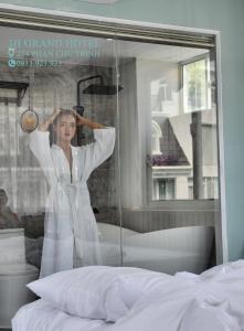 a woman is drying her hair in front of a bedroom at 3H Grand Hotel in Vung Tau